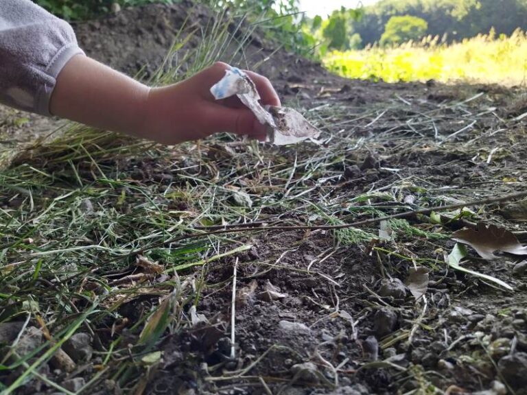 Hand hebt Müllstück vom Boden Polsum Naturfläche auf